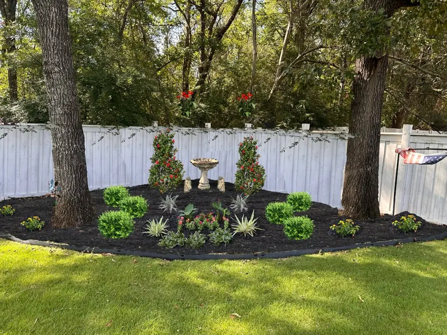Mulched bed with plants in front of a white fence